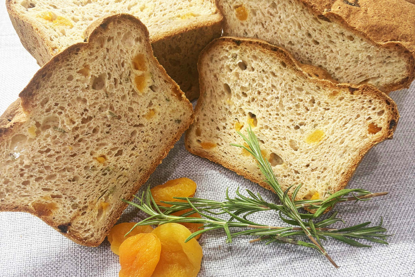 Slices of gluten-free bread with apricots and rosemary on a textured surface